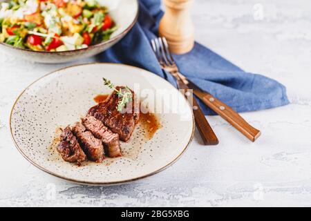 Sliced Grilled steak and vegetable salad on light background. Table setting, food concept. Stock Photo