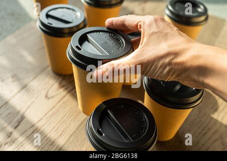 Woman taking a disposable cup of coffee on a wooden table. Brown paper cup with black lid Stock Photo