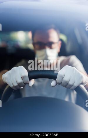 Close up of driver in protective mask with hands in rubber gloves on steering wheel, covid-19 protection from bacteria and virus infection. Stock Photo