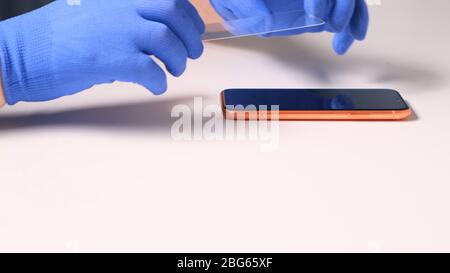 male hands in blue gloves replaces a broken tempered glass screen protector for a smartphone. A man prepares a smartphone to replace glass. Smartphone Stock Photo