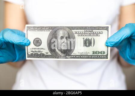 100 US dollars banknote held in hands in hands in blue disposable protective rubber gloves Stock Photo