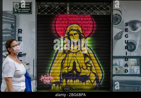 Caracas, Miranda, Venezuela. 18th Apr, 2020. Graffiti of the Virgin Mary on a Caracas street as a woman wearing the obligatory mouthpiece passes by because of the Covid-19 pandemic Credit: Jimmy Villalta/ZUMA Wire/Alamy Live News Stock Photo