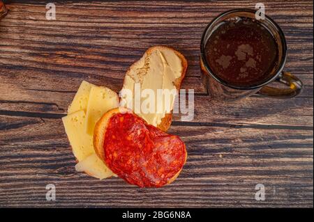 fresh wheat toast with butter, sausage and cheese and a mug of tea on a wooden background. Close up Stock Photo