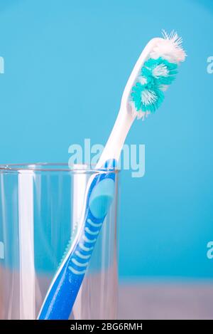 Old used toothbrush in a glass cup on a blue background close-up Stock Photo