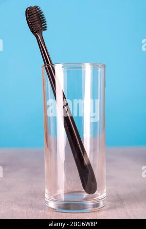 Black toothbrush in a glass cup stands on a table on a blue background Stock Photo
