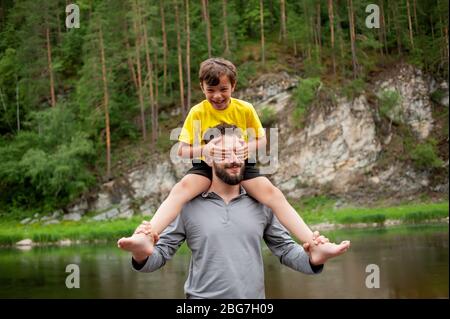 Father and son are smiling while spending time together. Little boy sits on father neck Stock Photo
