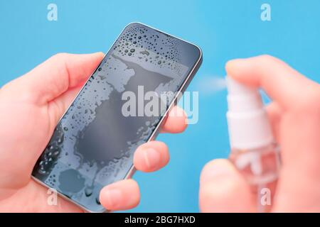 Close-up hands clean mobile phone on blue background. Closeup of a Doctor in gloves disinfecting his smartphone. Hands wiping mobile phone with Stock Photo