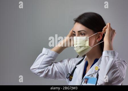 Woman healthcare professional demonstrating proper donning of mask for protection from coronavirus. Up close female healthcare worker putting on safet Stock Photo
