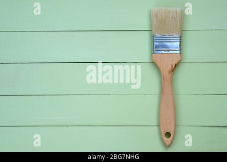 Paint brush with bristles and a wooden handle on a green background. Wooden pale green boards background top view. Wooden painted planks and a small b Stock Photo