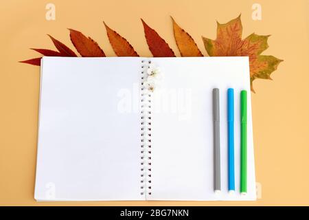A notebook with blank white sheets is opened in the middle of a top view. Notepad for notes and sketches and colored markers. Autumn is the time to go Stock Photo