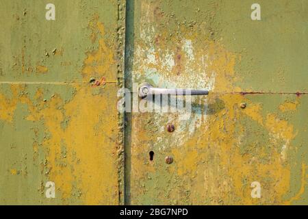 Green door of metal gate with aluminum handle close-up. Metal surface with peeling faded green paint background. Stock Photo