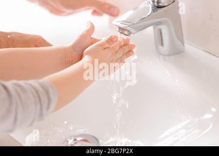 A young child washes his hands under running water. Stock Photo