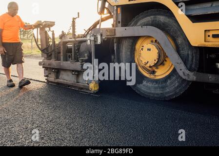 Highway Road worker operating asphalt machine laying new asphalt or bitumen during highway construction Stock Photo