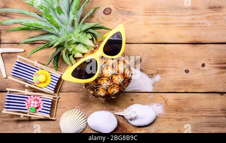 Pineapple with sunglasses on wood background. Creative minimal summer holiday concept with miniature toy. Stock Photo