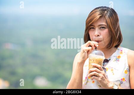 The hands of a woman holding iced coffee and drinking Background blurry views tree Stock Photo