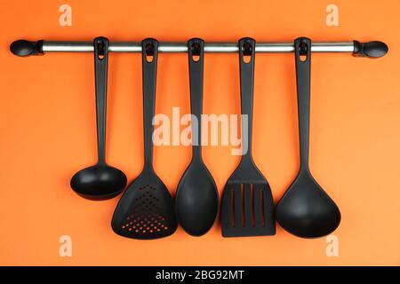 Plastic kitchen utensils on silver hooks on orange background Stock Photo