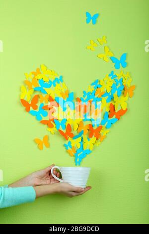 Paper butterflies fly out of cup on green wall background Stock Photo
