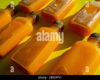 Orange juice iced cold in the bottles. Close-up square shape bottle with cold orange juice on yellow background. Stock Photo