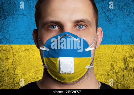 Young man with sore eyes in a medical mask painted in the colors of the national flag of Ukraine. Coronovirus disease  COVID-19 concept.  Man is afrai Stock Photo