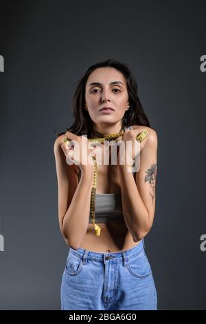 Sick woman with measuring tape on grey background. Concept of