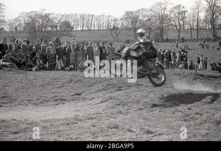 1960s, historical, spectators standing on a hilly ridge, watching an off-road motorcycle scramble race, a sport which later became commonly known as motorcross racing. The first ever official scramble was held in Camberley, Surrey, in 1924. Post-WW2 the sport expanded as motorbikes became lighter and faster. Stock Photo