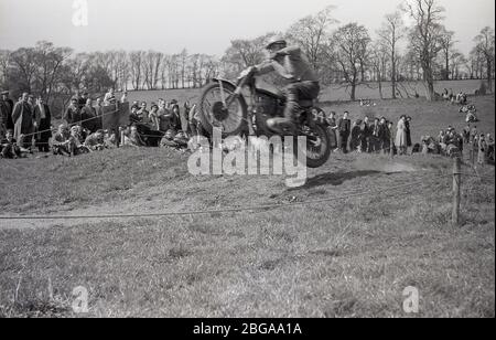 1960s, historical, spectators standing on a hilly ridge, watching an off-road motorcycle scramble race, a sport which later became commonly known as motorcross racing. The first ever official scramble was held in Camberley, Surrey, in 1924. Post-WW2 the sport expanded as motorbikes became lighter and faster. Stock Photo