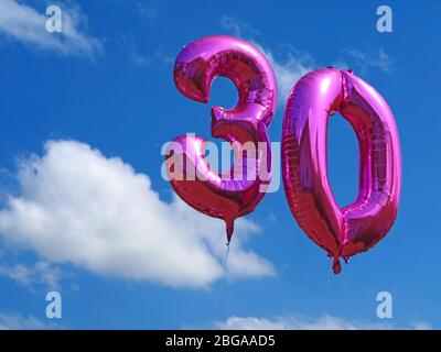 pink helium balloons on blue cloudy sky, celebrating the age thirty with number balloons, birthday background Stock Photo
