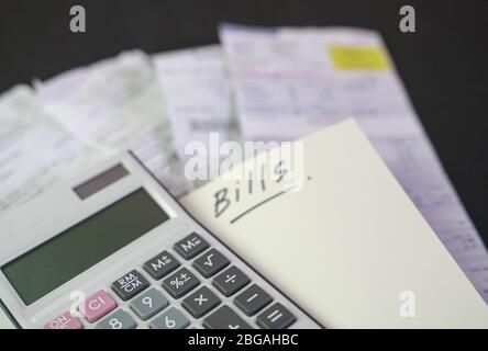 Calculator on top of notepad with the words Bills. Stack of bills at the background. Copy space. Stock Photo