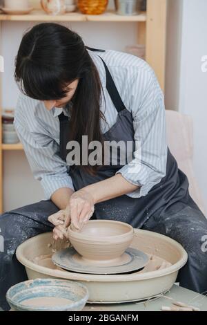 Woman shaping clay bowl on a pottery wheel in her private workshop Stock Photo