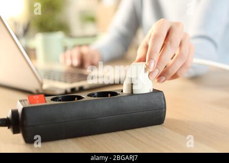 Close up of woman hand using laptop plugging plug on a power strip socket on a desk at home Stock Photo