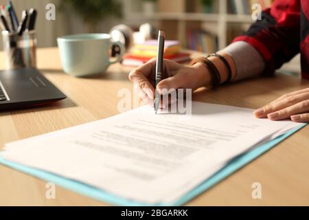 Close up of student girl hand signing contract on a desk at home at night Stock Photo