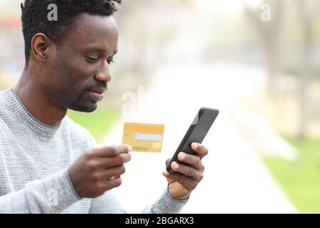 Black man paying with credit card online on smart phone outdoors in a park Stock Photo