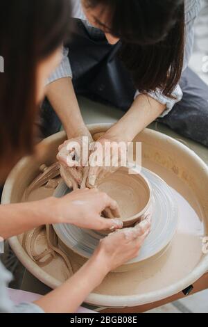 Two women working on a clay bowl on a pottery wheel in a private workshop Stock Photo