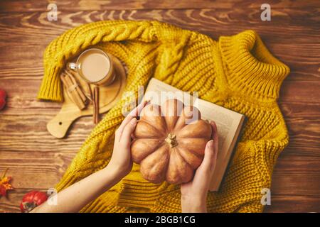 Mug of coffee, cozy knitted jacket, autumn, open book and pumpkin on wooden board. Fall still life, vintage style. Flat lay. Stock Photo