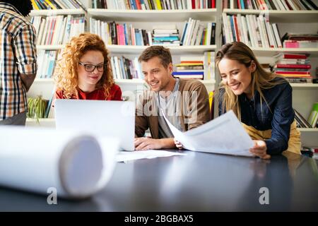 Young architect colleagues are analyzing blueprints while working on a new project Stock Photo