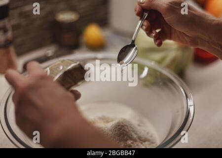 Process of adding yeast to a dough mixture, hands holding small sachet and spoon Stock Photo