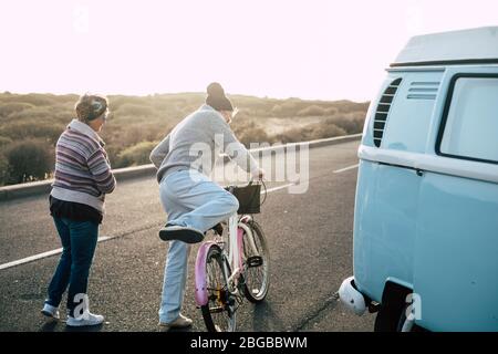 Old modern senior couple viewed from back enjoy the outdoor leisure activity together - bike and van for transport concept - sun  and sunlight in back Stock Photo