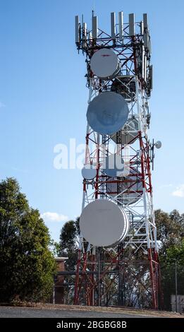 Communications radio tower with satellite dish mobile cell phone against blue sky Stock Photo