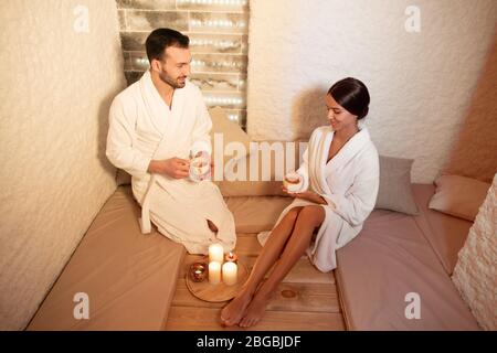 Man and a woman drinking wellness tea in a salt room by candlelight. Couple enjoys relaxation at the spa Stock Photo