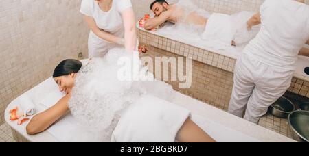 Mixed race couple is having fun and relaxing in a Turkish bath during a foam massage procedure. Hammam workers wash their bodies with soap and foam Stock Photo
