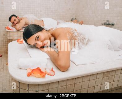 Beautiful woman and her boyfriend lie on hot hammam massage tables before body wash procedures. Turkish bath for couple Stock Photo
