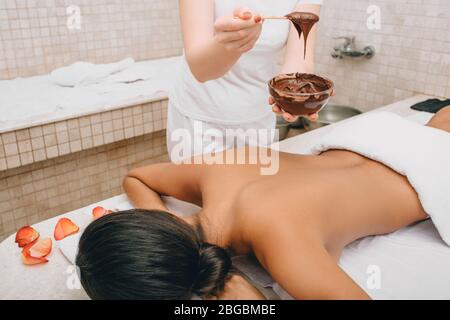 Chocolate wrap in the spa. Young woman getting a chocolate mask on her body to moisturize her skin Stock Photo