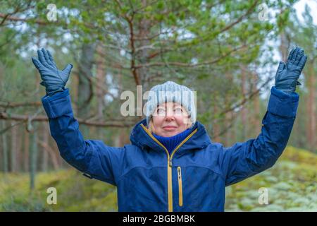 Portrait of excited woman holding hands up. Walk in the park. Pine tree background. Spring holidays vacation trip concept. Stock Photo