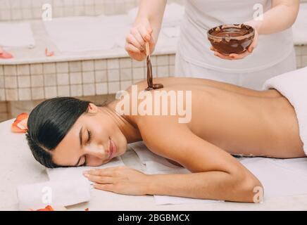 Chocolate wrap in the spa. Young woman getting a chocolate mask on her body to moisturize her skin Stock Photo