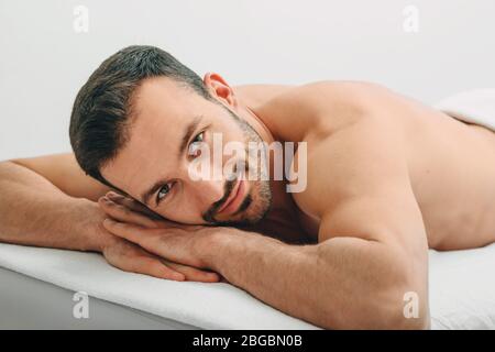Portrait of a brunette man lying on a massage table, who is smiling, looking at the camera after massage. Spa and resort Stock Photo