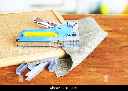 Construction stapler with staples and cork board on table on bright background Stock Photo