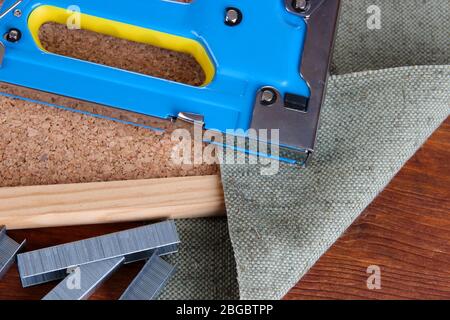 Construction stapler with staples and cork board on wooden background Stock Photo