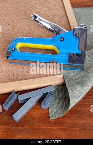 Construction stapler with staples and cork board on wooden background Stock Photo