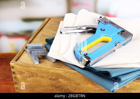 Construction stapler with fabrics and staples on wooden box on bright background Stock Photo
