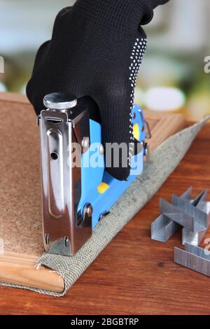 Fastening fabric and board using construction stapler on bright background Stock Photo